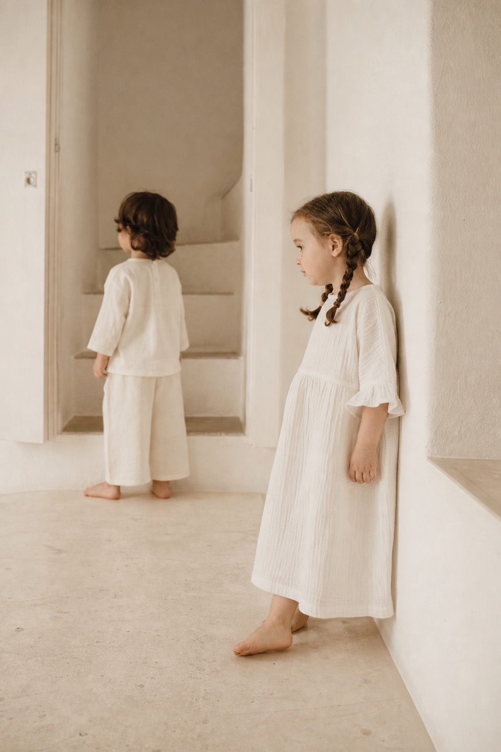 Two children in natural linen clothing in a whitewashed Mediterranean interior